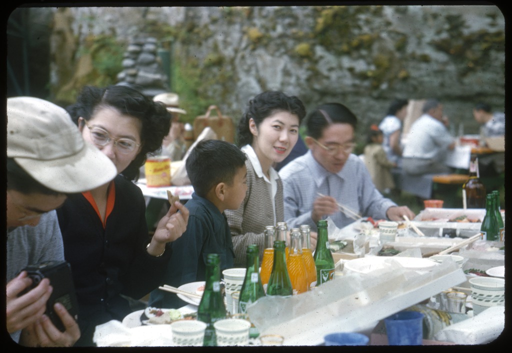 Color slide of people sitting around a picnic table at a community picnic. From left to right: Ted Tamaki, Shizuko "Shiz" (Ochiai) Ota Okazaki, Eddie Tamiyasu, Nobuko (Ochiai) Susaki, and unidentified. According to donor processed on September 12, 1952. 