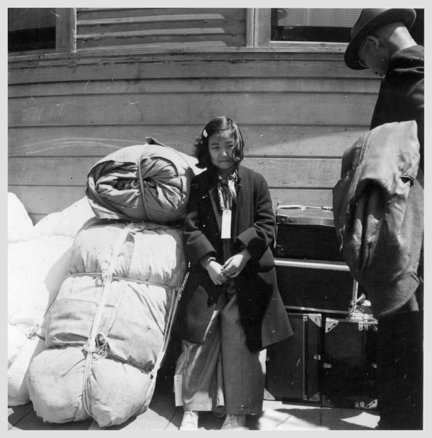 Oakland, Calif. (Oak Street)-- Young evacuee, Kimiko Kitagaki,11, of Japanese ancestry guarding the family belongings near the WCCA Control Station at 1118 Oak Street in Oakland, Calif. In half an hour the evacuation bus will depart for Tanforan Assembly center. and from there to a permanent detention center in the Utah desert at Topaz Interment Camp. Photographer: Lange, Dorothea -- Oakland, California. 5/ 6/ 42 Contributing Institution: UC Berkeley, Bancroft Library