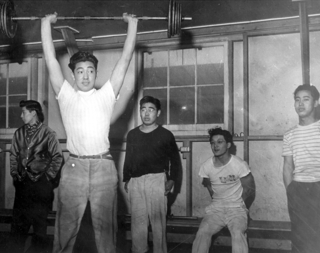 Kaz Tsujikawa lifts weights as his friends look on.