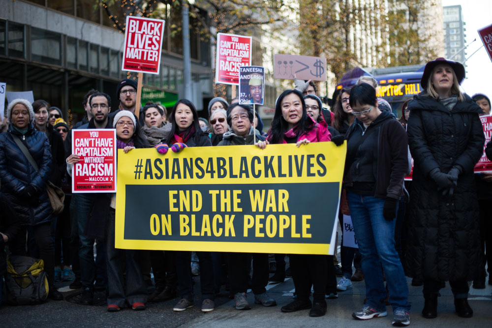 Asian Americans at a protest holding a banner that reads "Asians 4 Black Lives: End the War on Black People."