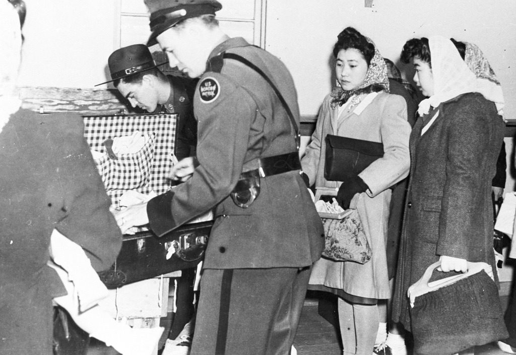 Original WRA caption: Border patrolmen, under the direction of the Department of Justice, inspect the baggage of women going to Crystal City, Tex. Internment Camp.