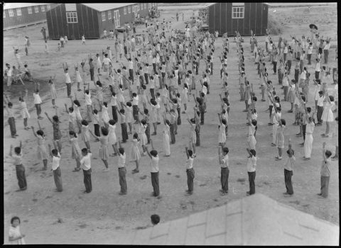 Japanese American students lined up doing calisthenics exercises outside barracks at Jerome concentration camp