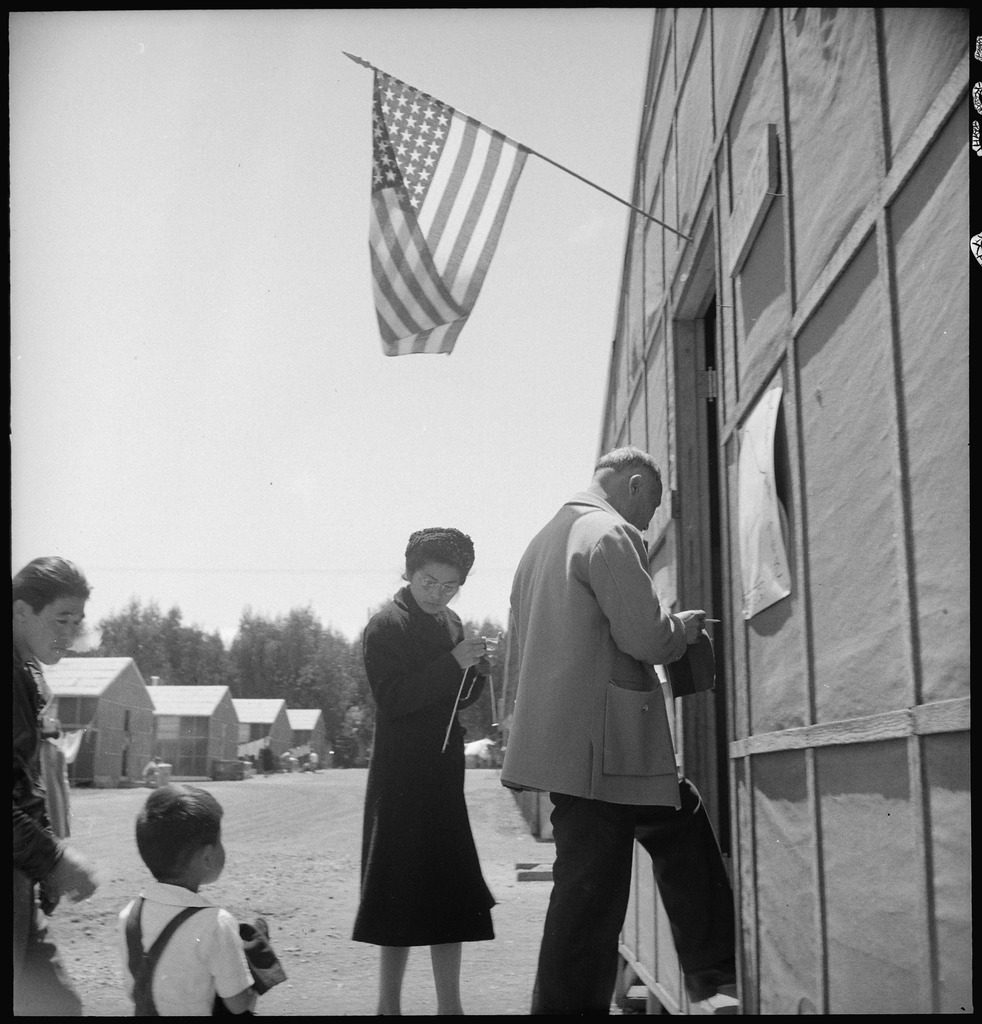 Japanese Americans enter the Recreational Hall at Tanforan to cast votes for the Tanforan Assembly Center Advisory Council. An American flag flies over the doorway.