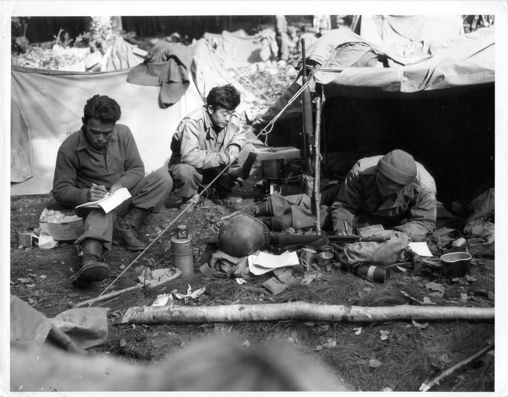 Three Japanese American soldiers writing letters in a bivouac.