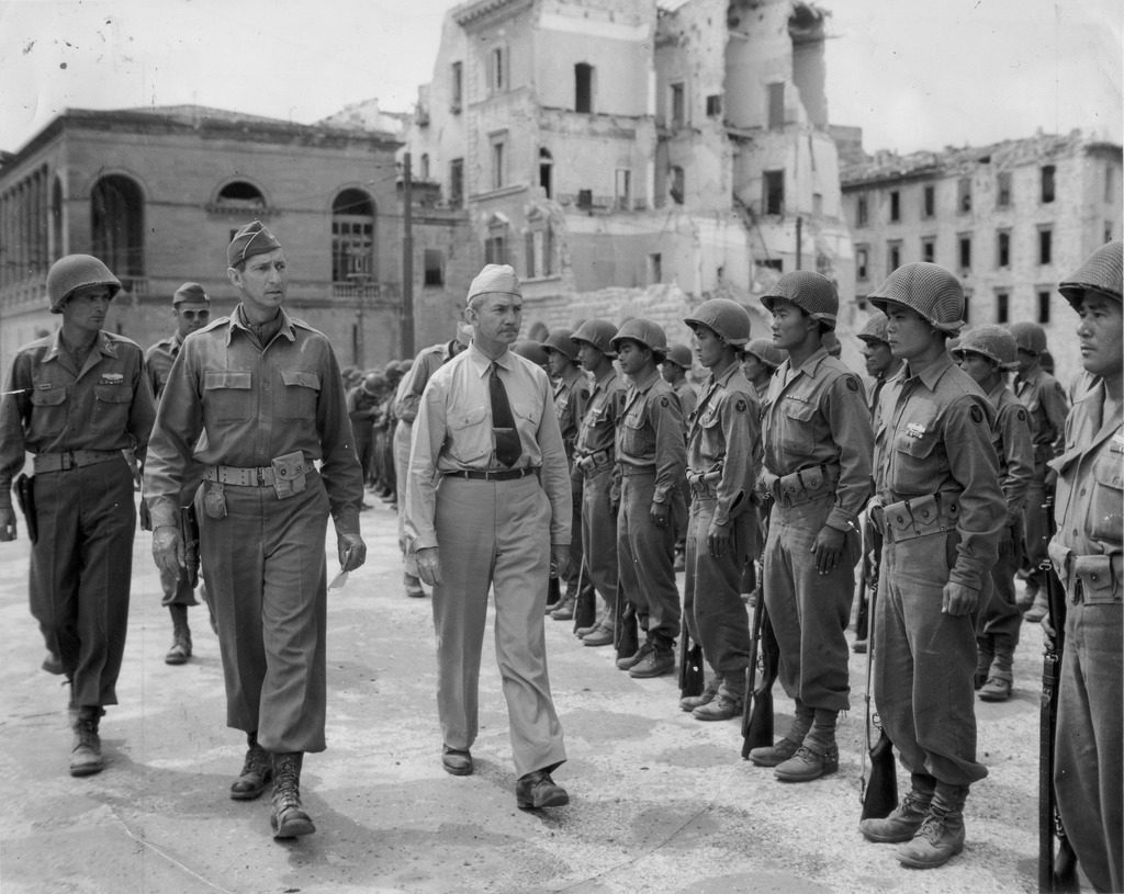 With the wreckage of Bighorn in the background, Lieutenant General Mark W. Clark and Secretary of the Navy James V. Forrestal inspect troops from the 100th Infantry Battalion composed of Americans of Japanese descent.