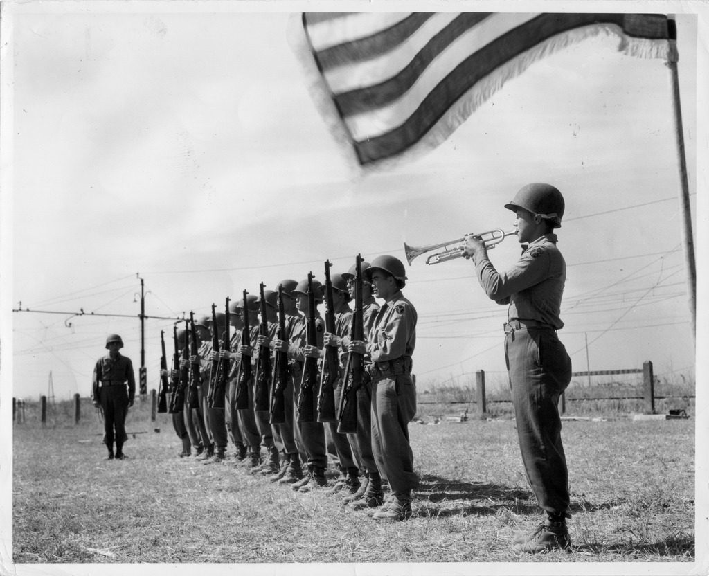 Charles Kimura plays taps as the rifle squad stands at "present arms," after firing salute to the 72 soldiers of the 442nd honored at a memorial service held after one month of combat.