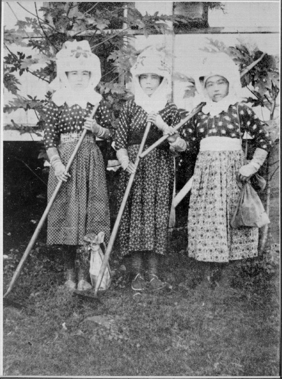 Three Japanese women laborers on a Hawaiian plantation, holding hoes and wearing protective clothing.