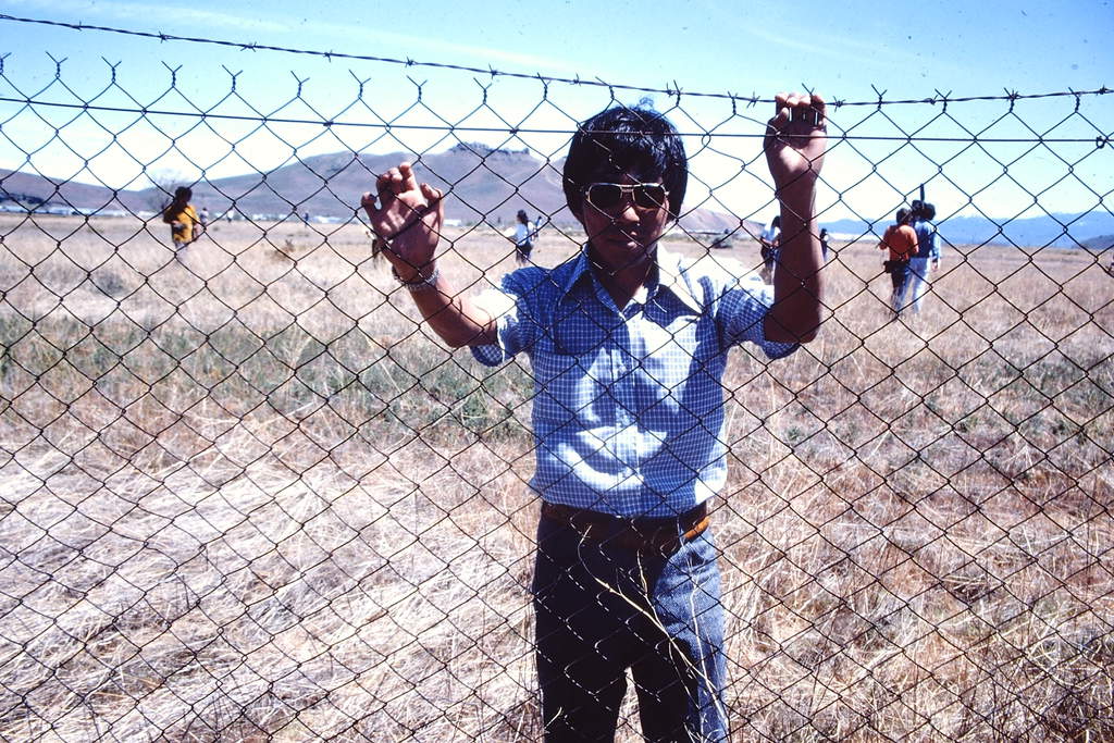 A man behind barbed wire at Tule Lake, with Castle Rock in the background, at the 1974 pilgrimage