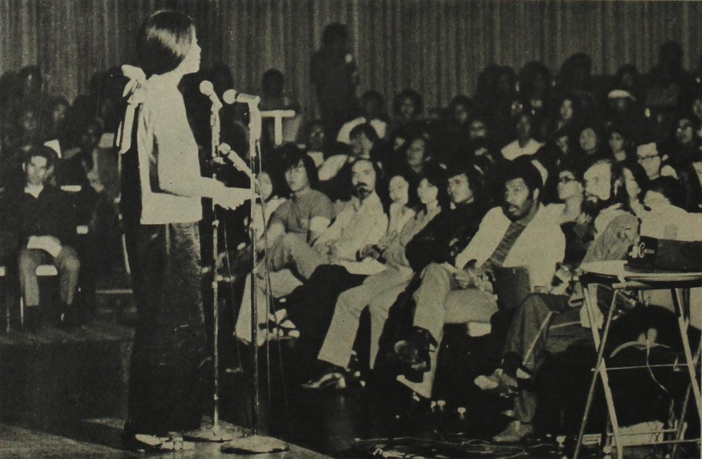Activist Pat Sumi speaking into a microphone in front of an audience at an anti-war event in Los Angeles in 1971.