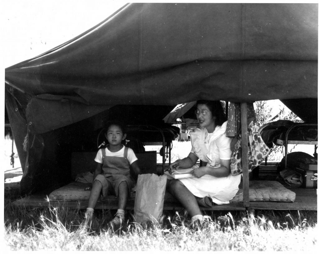 A Japanese American woman and child sitting inside a tent in a farm labor camp.