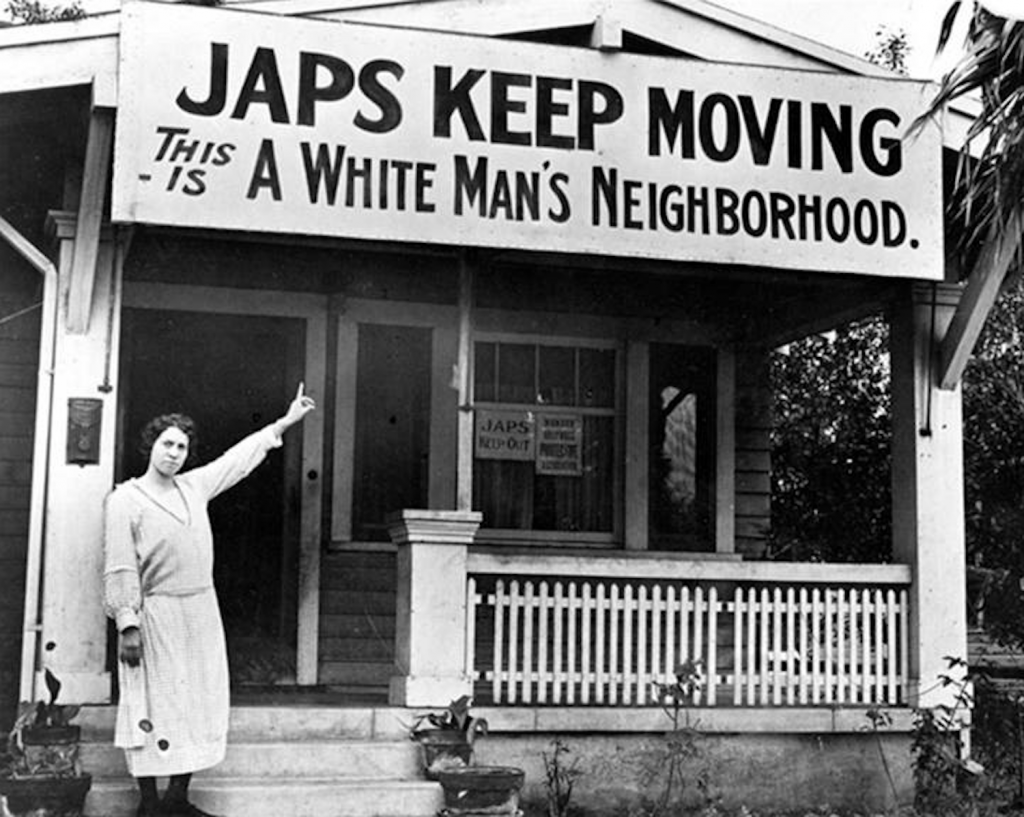 Photo of a white woman standing in front of a house and pointing at a large sign over the porch that reads "Japs Keep Moving - This Is a White Man's Neighborhood."