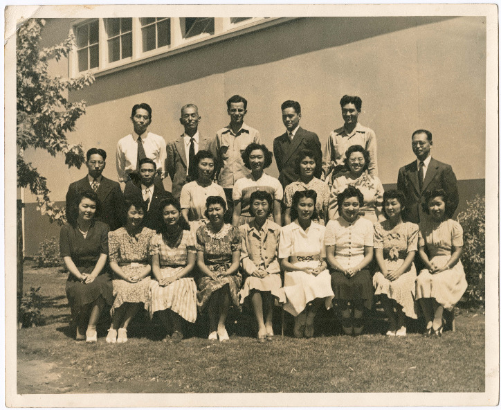 A group photo of Japanese Americans at the Merced Assembly Center. A row of women are seated in front, and two rows of men and women stand behind them.
