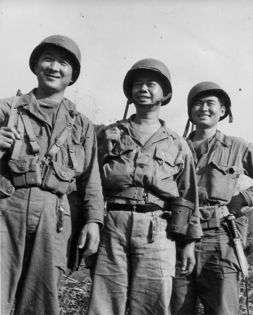 Three Japanese American soldiers in Myanmar during WWII. They are wearing army uniforms with helmets, and standing side by side.
