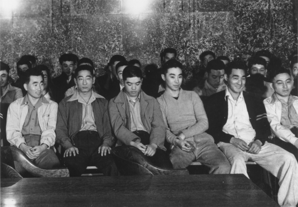 Black and white photo of Japanese American WWII draft resisters seated inside a courtroom.