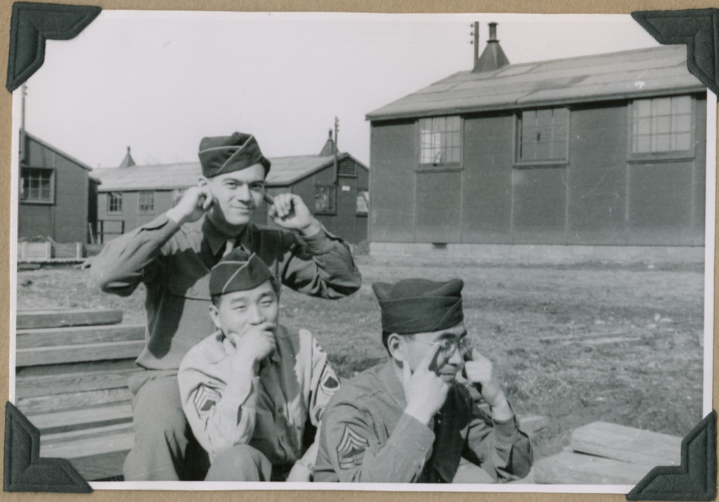 Three soldiers striking a "Hear no evil, speak no evil, see no evil" pose outside barracks. They are sitting in a row, with the soldier in front covering his eyes, the soldier in the middle covering his mouth, and the soldier in the back plugging his ears.