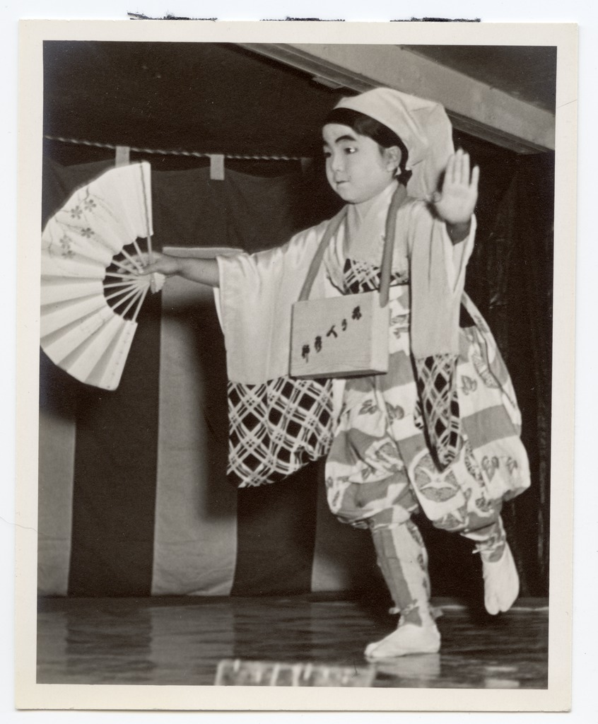 A Japanese American child in traditional costume performing a Japanese dance.