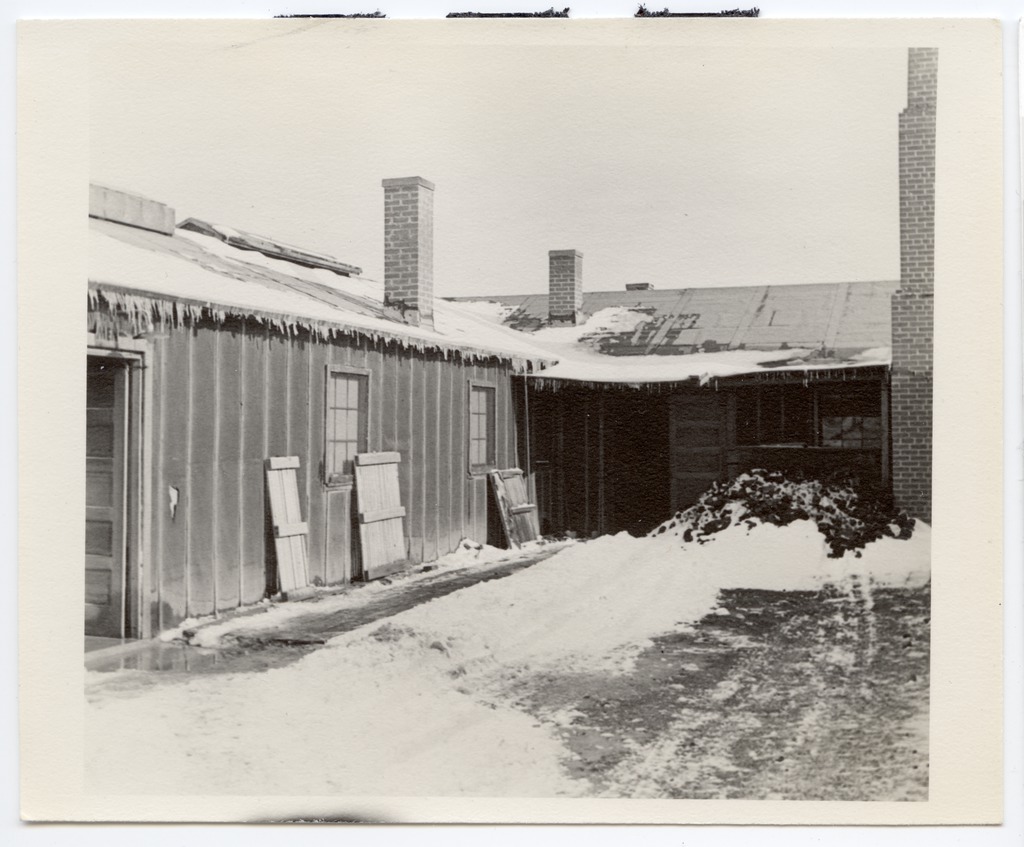 The outside of a latrine in Heart Mountain. There is snow piled up on the ground and icicles hanging off the roof.