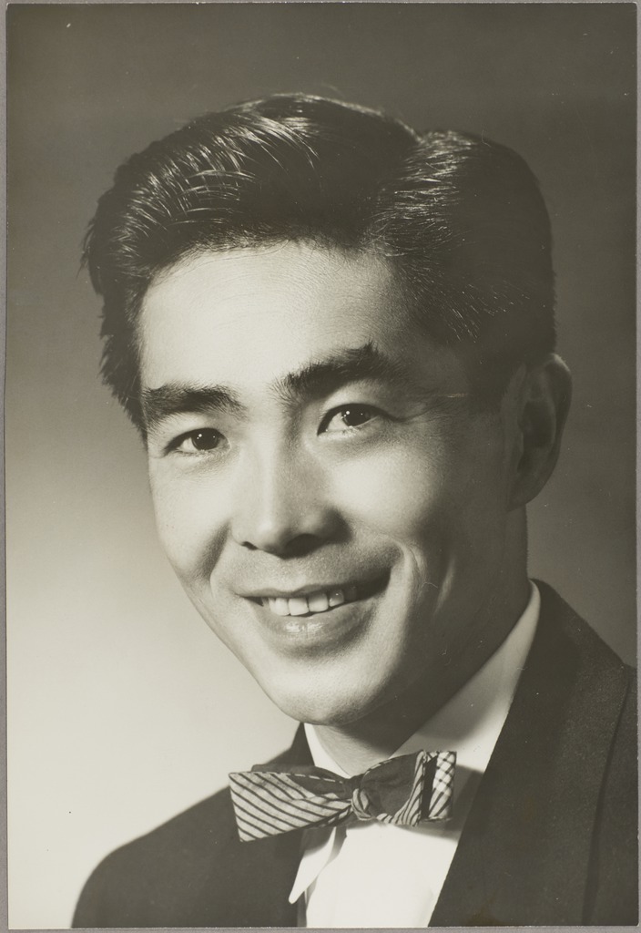 Black and white portrait of Masato Doi. He is wearing a suit and bow tie, and smiling at the camera.