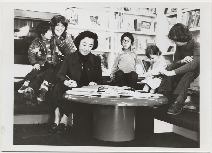Yoshiko Uchida sitting at a table signing books. Two women and three children are seated behind her.