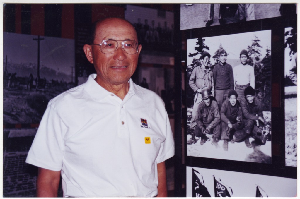 Fred Shiosaki standing next to a photo of himself and fellow Nisei soldiers taken during WWII.