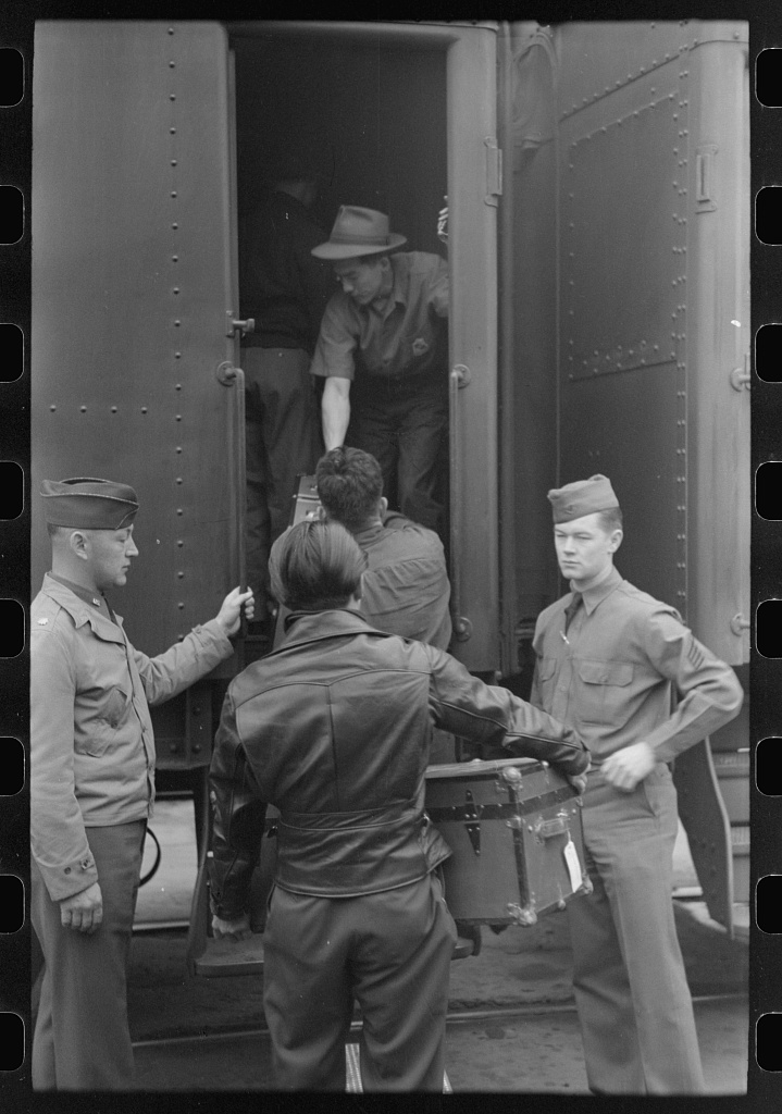 Three Japanese Americans loading baggage onto a train while two soldiers look on.