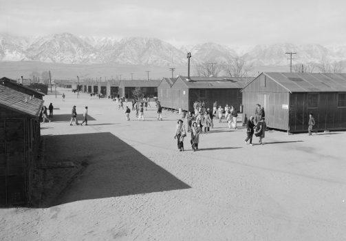Japanese Americans walking between barracks at Manzanar. The Sierra Nevada mountains are visible in the distance.