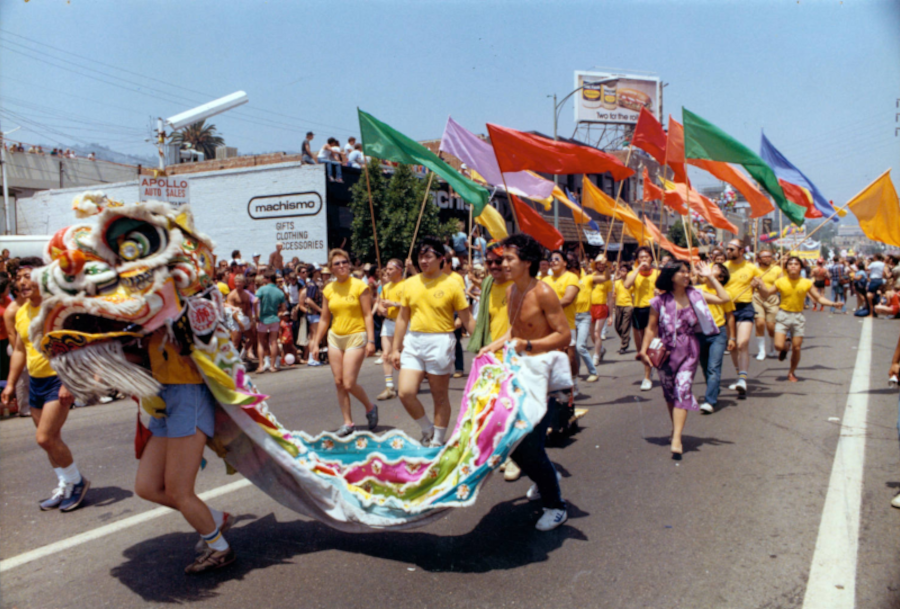 Members of Asian/Pacific Lesbians and Gays marching in the Los Angeles Pride Parade in 1982. Two lion dancers are leading a group of marchers wearing yellow t-shirts and carrying colorful flags.