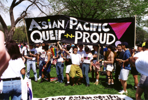 A group of cute and happy queers standing under a banner that reads "Asian/Pacific Queer n Proud"