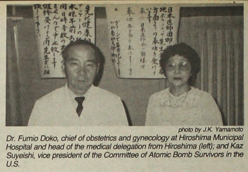 Hibakusha activist Kaz Suyeishi and a physician from Hiroshima standing in front of two posters with Japanese writing. The caption reads, "Dr. Fumio Doko, chief of obstetrics and gynecology at Hiroshima Municipal Hospital and head of the medical delegation from Hiroshima (left); and Kaz Suyeishi, vice president of the Committee of Atomic Bomb Survivors in the U.S."