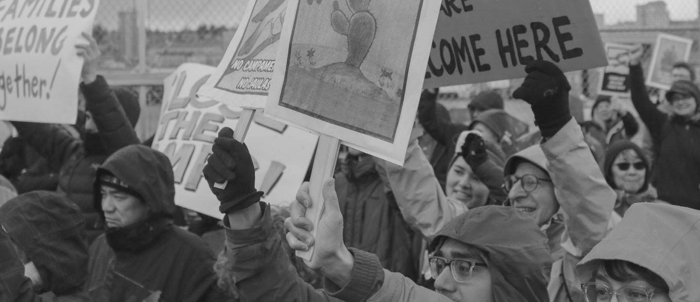 Protesters wearing rain jackets hold signs at a rally outside of the Northwest Detention Center.