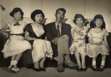 Japanese American family in the 1950s sit on a couch and pose for a photo
