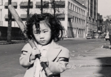 Young Japanese American girl stands on a sidewalk, holding a baseball bat
