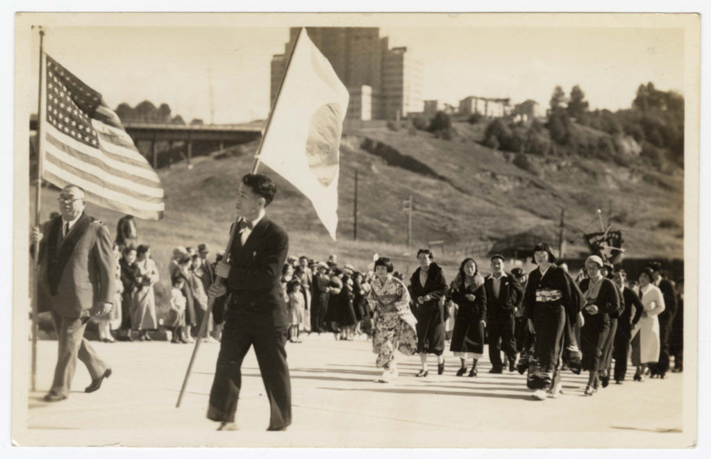 Two men hold American and Japanese flags at the front of a procession moving the Seattle Buddhist Betsuin Temple’s butsudan in 1933.