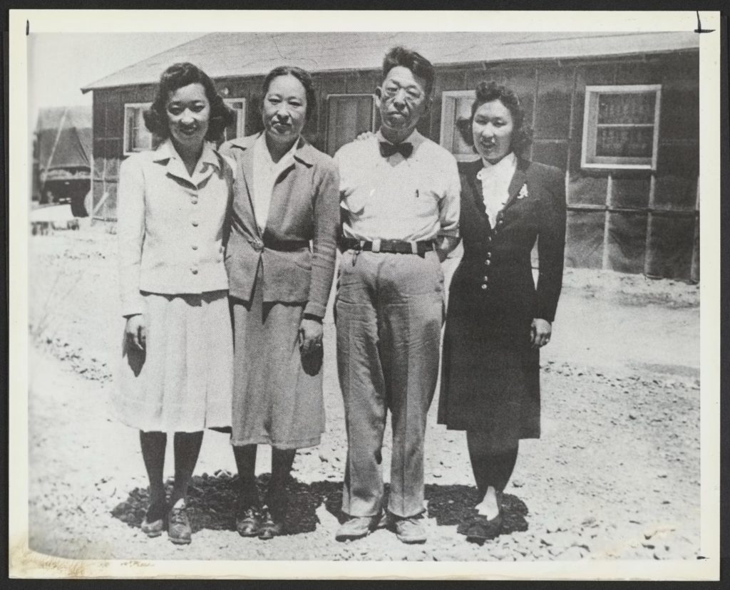 The Uchida family at Topaz concentration camp in 1943. They are standing in front of a barrack, from left to right: Yoshiko, Iku, Dwight, and Keiko.
