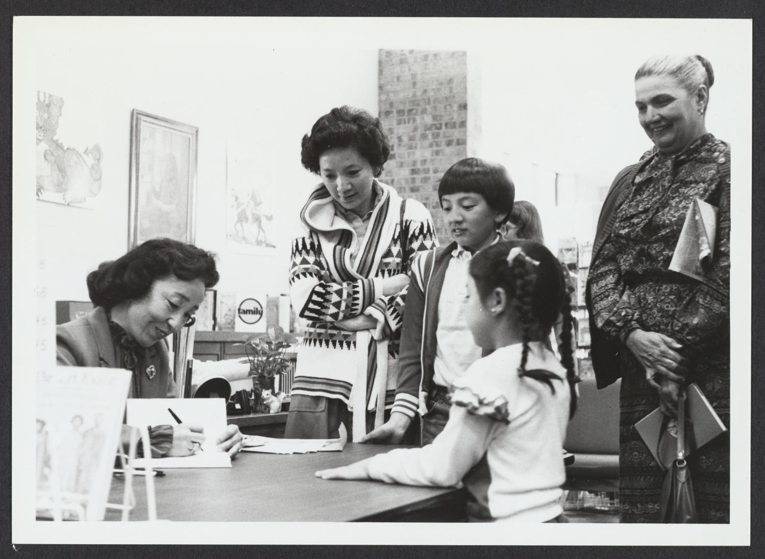 Yoshiko Uchida signing a book for a young Asian girl while two adults and an older boy look on.