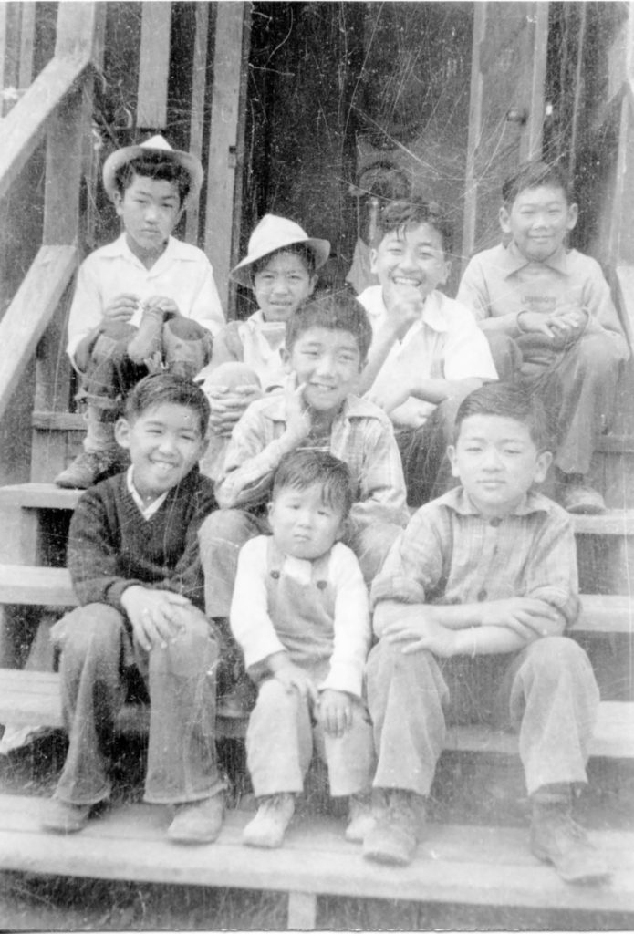 Eight incarcerees on steps of the Manzanar Children’s Village sit outside on steps.