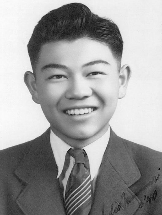 Portrait of Sadao Munemori. He is smiling and wearing a suit and tie.