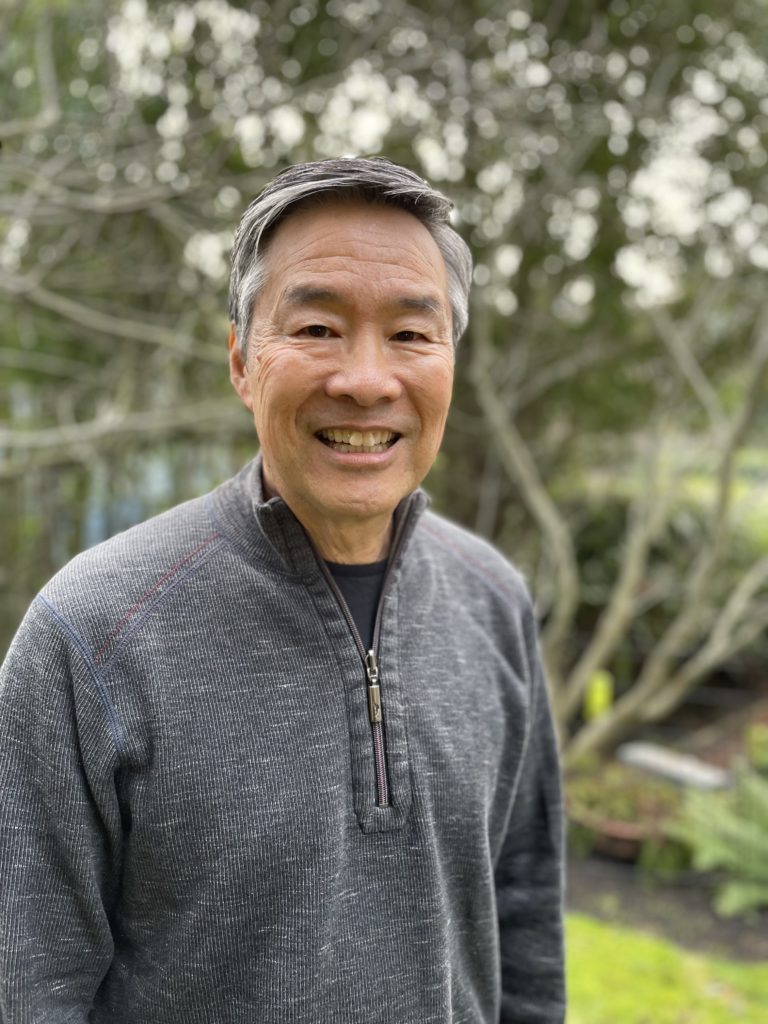 Tom Ikeda smiling in front of a garden.