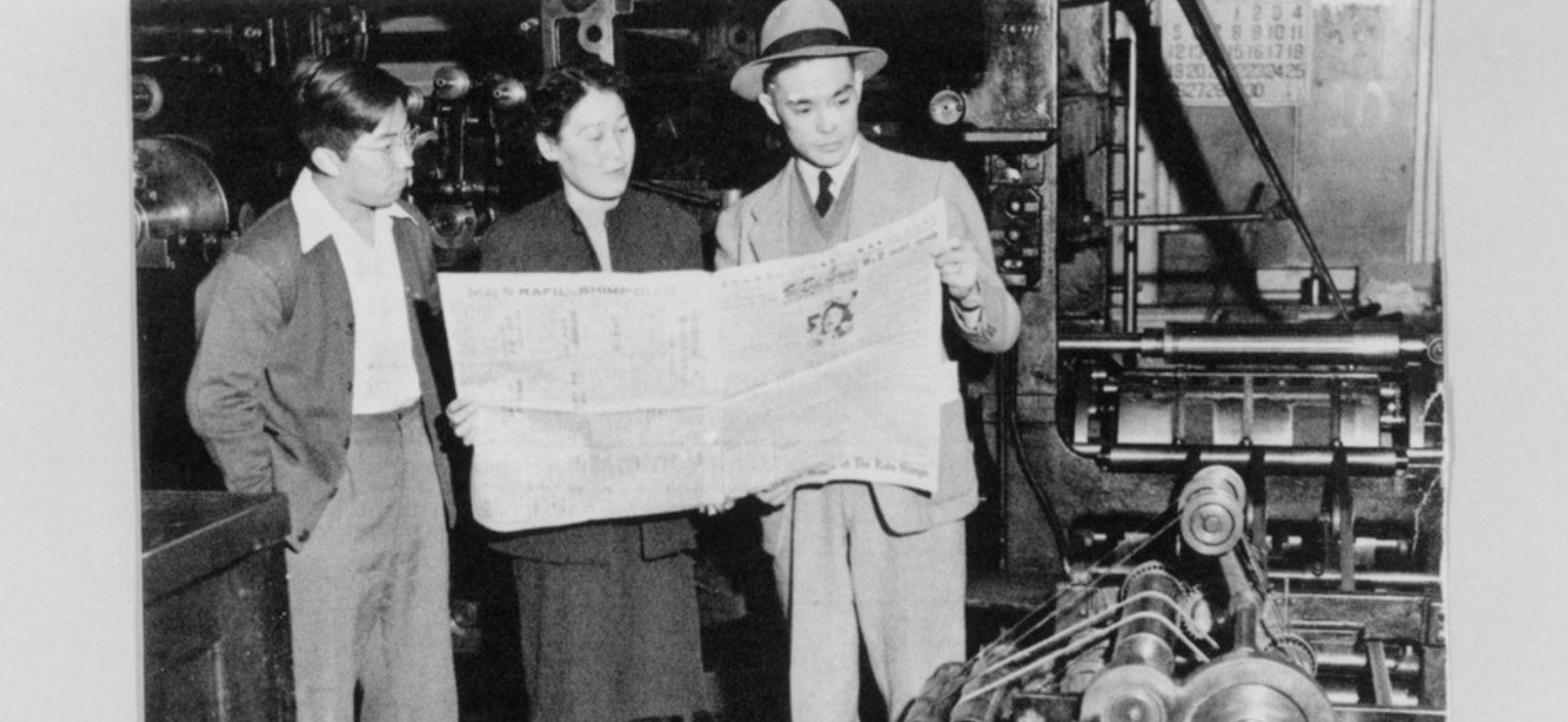 Three Japanese Americans reading a newspaper.