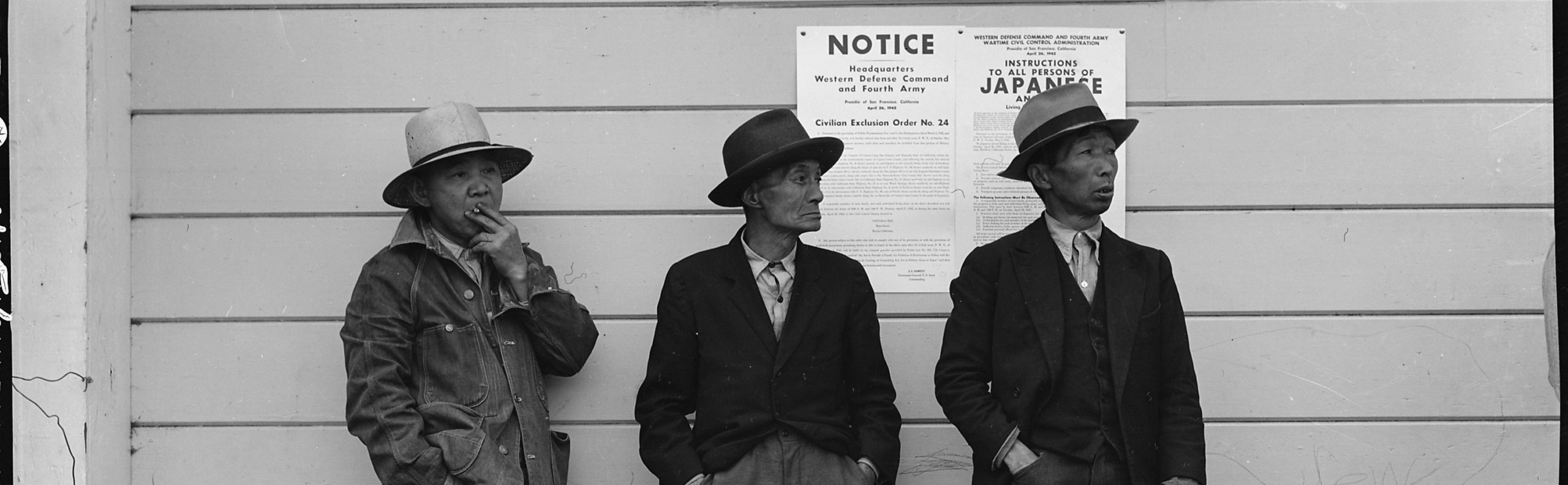 Three Japanese American men standing in front of a wall with posted exclusion orders.