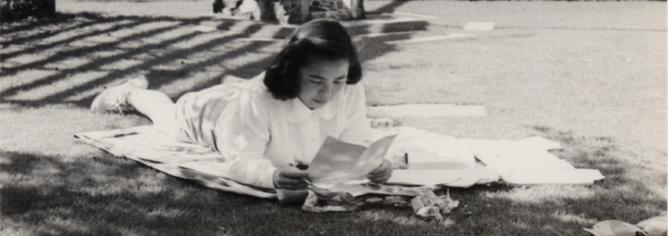 Japanese American girl lying in the grass and reading.