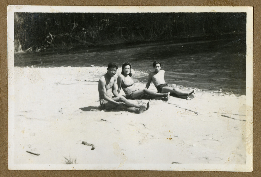Two Japanese Peruvian men and a Peruvian woman sitting on a riverside. wearing bathing suits.