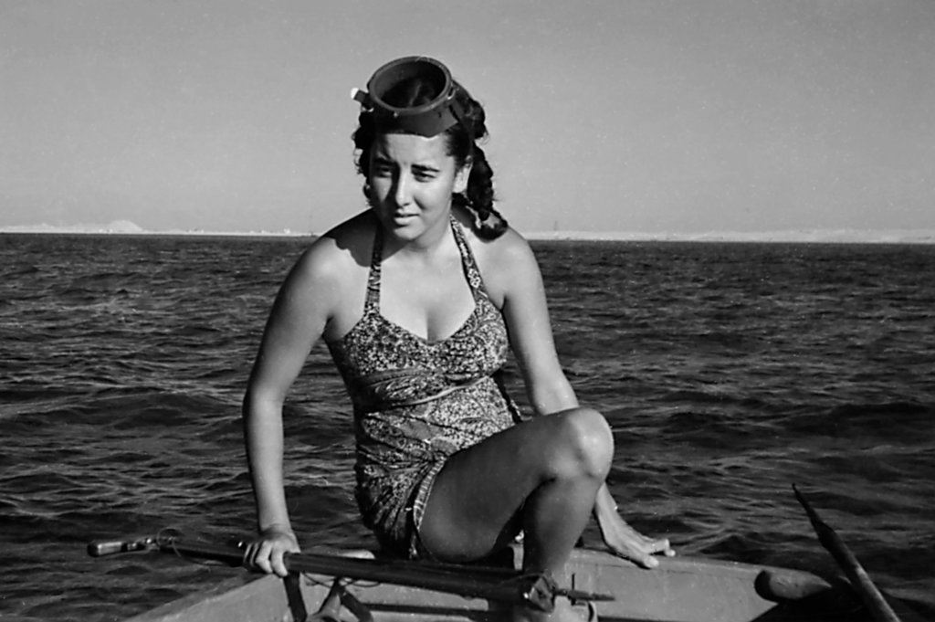 Eugenie Clark sitting on a boat holding what appears to be a spear gun in 1951.
