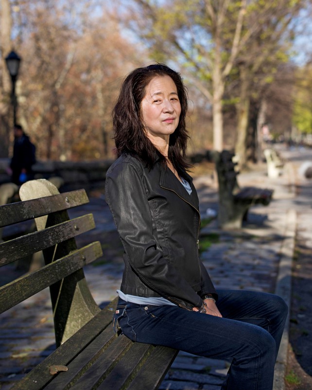 Author Julie Otsuka sitting on a park bench in jeans and a black leather jacket.