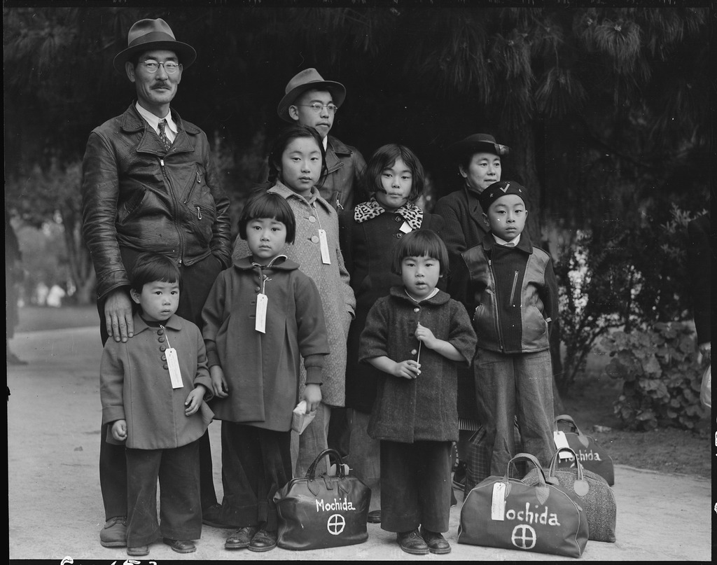 Japanese American family wearing evacuation tags and waiting with their luggage to be removed to a concentration camp.