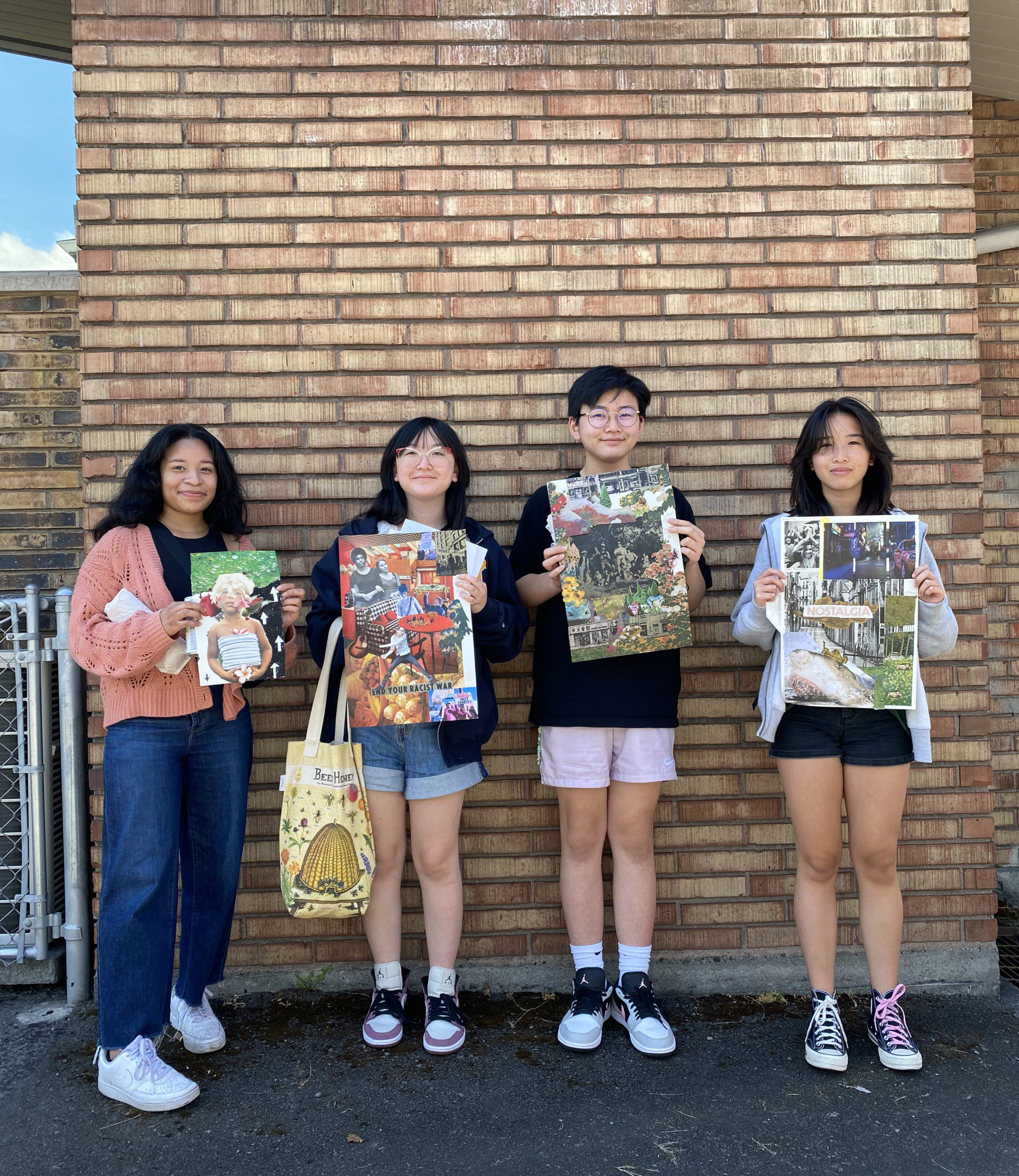 Four teens standing against a brick wall outside the Densho building holding collages they made inspired by Gidra.