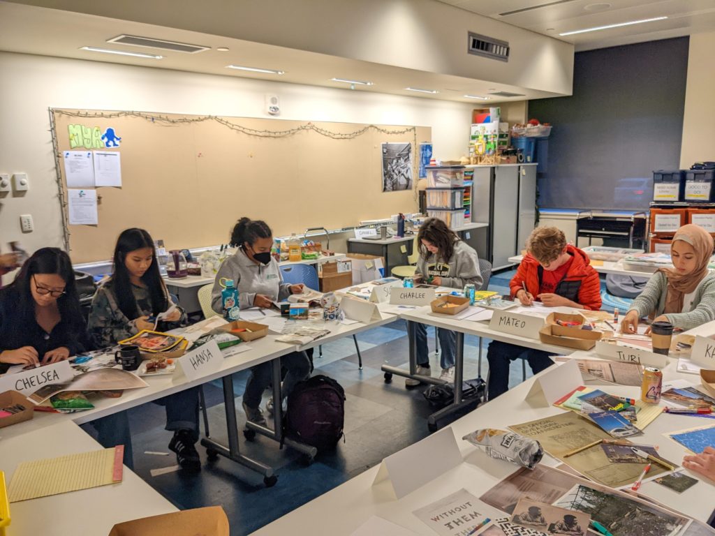 Six teens sitting around tables working on collages.