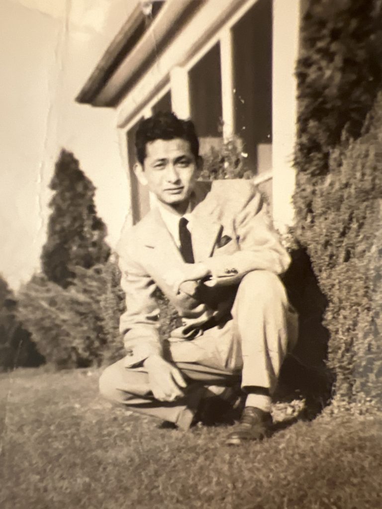 Seiichi Ichikawa posing in front of a home wearing a well-tailored suit with a pocket square. 