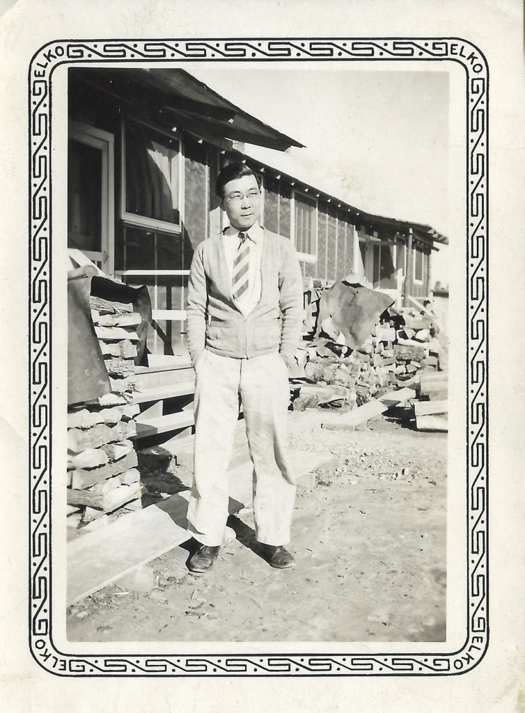 John Yasui standing in front of barracks inside a concentration camp in 1942.