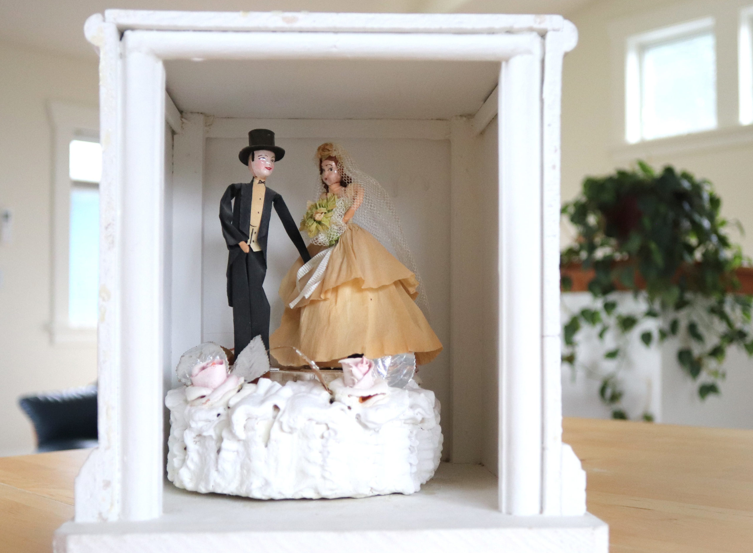 The top tier of the Nishimotos' wedding cake inside a display box. On top of the cake are a set of wooden bride and groom figures.